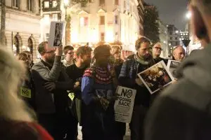 A photograph of members of audience holding placards from demonstrations. The main poster says No Going Back! There are about 10 people in the photo.