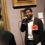 Rohit is speaking into a microphone in one of the galleries. He looks relaxed and confident. He is wearing a badge that says - End colonial anit queer laws - No 377! Defy the legacy of Babington Macaulay
