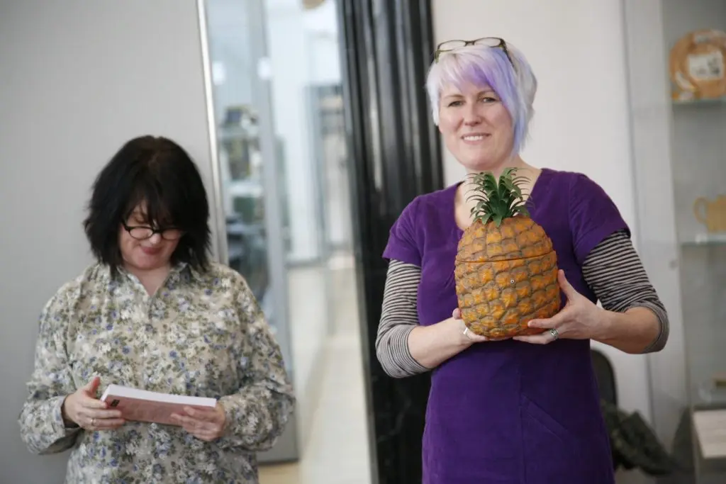 Ruth proudly holds up her plastic pineapple while Tracey Potts looks at the cover of her kitsch book