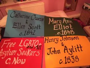 Four placards in bold colour from the rainbow flag. Each features the names of individual or groups of LGBTQI prisoners or detainees featured in the show.