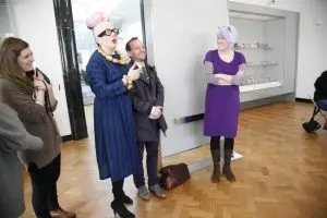 Long shot of the gallery with Birdie standing next to a grinning Lucas
